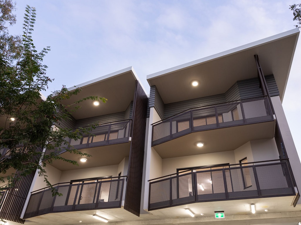 External view at dusk, showing 2 storeys of balconies with perforated metal screens, other vertical screening, and rendered blockwork.