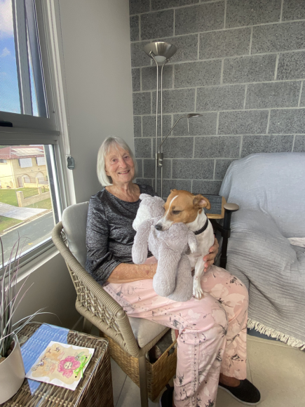Desley smiling on a chair with Millie, her small dog, on her lap