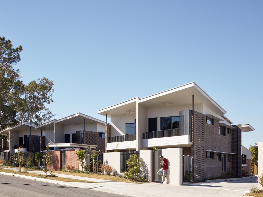 View from the street, showing the low-scale, townhouse-style buildings, with upper-level balconies facing the street. Building materials include brick, rendered blockwork, sheeting and metal. 