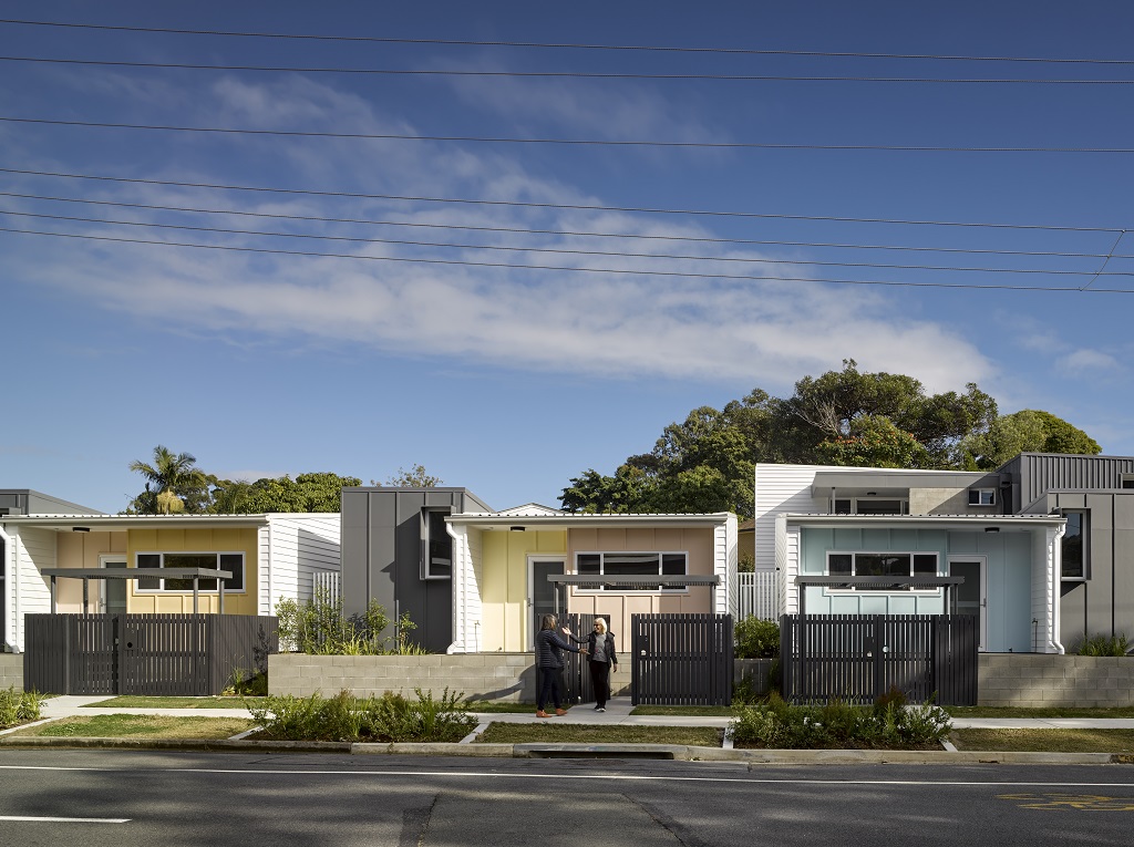 View from the street, showing low-set, lightweight dwellings in white and grey, with pastel-coloured features – a distinctly Gold Coast aesthetic.